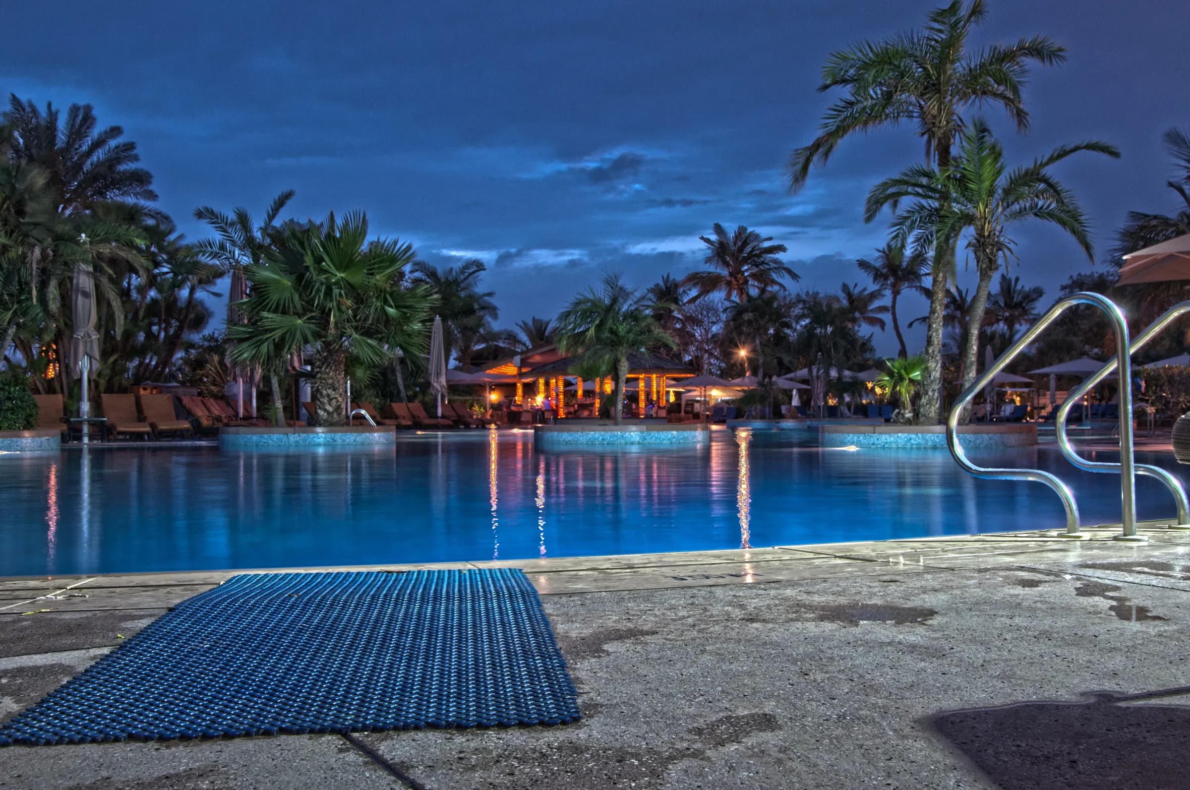 A palm-lined beach hotel pool on Jumeirah Beach at dusk
