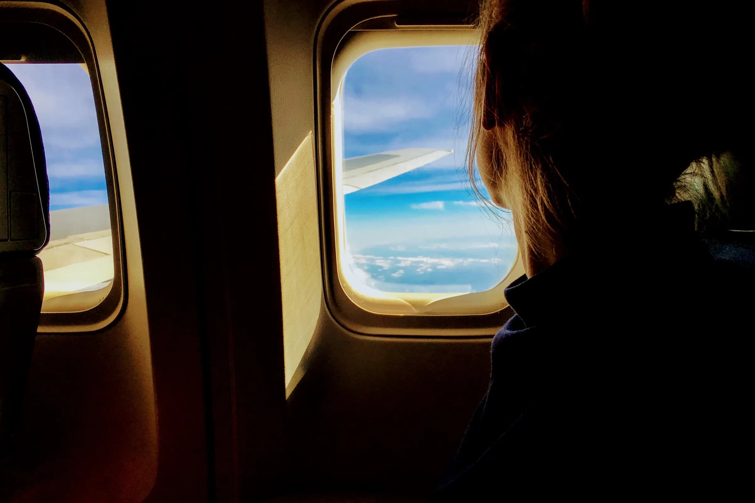 A traveller looking out of a plane window above the clouds